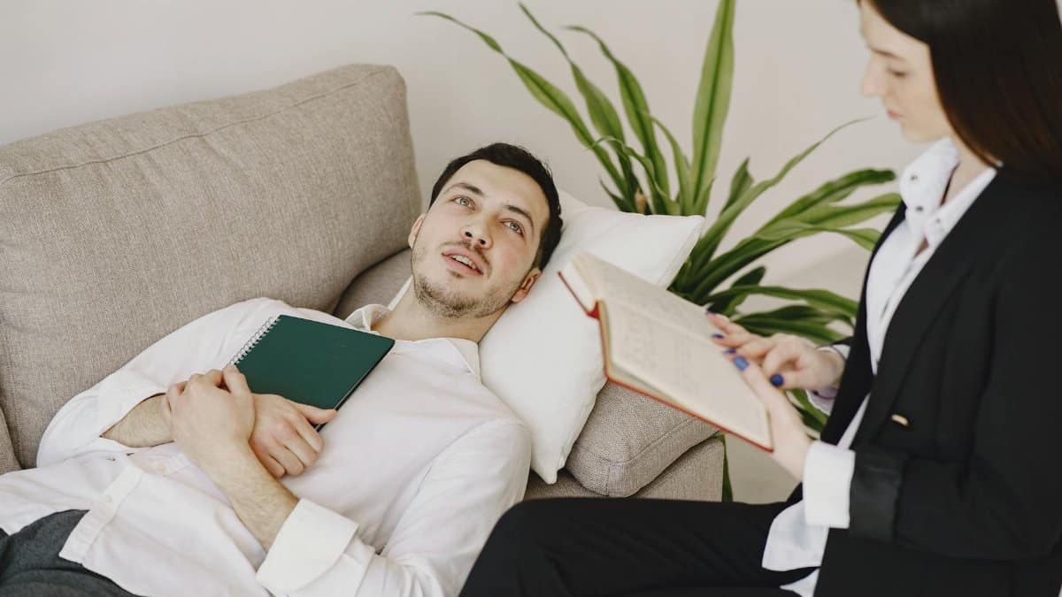Thoughtful well dressed man with journal lying on sofa in office of modern female therapist and telling about problems