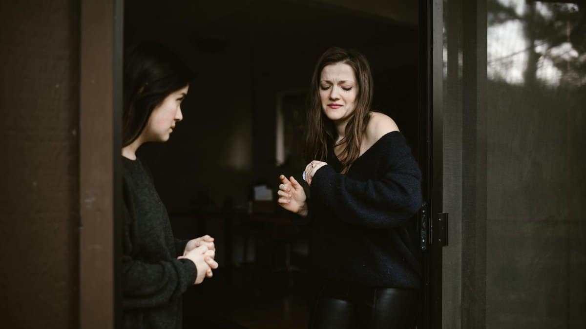 Two women in an emotional conversation at a doorway, highlighting tension.