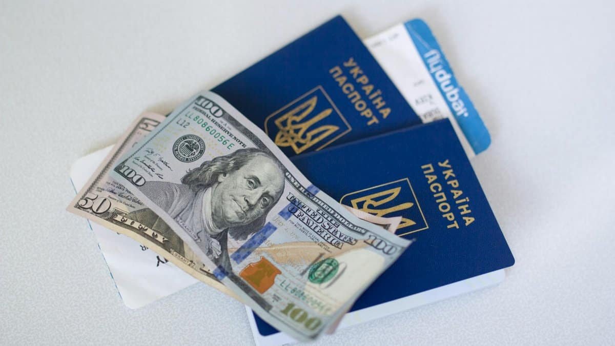 Close-up view of Ukrainian passports with US dollar bills, symbolizing travel readiness.