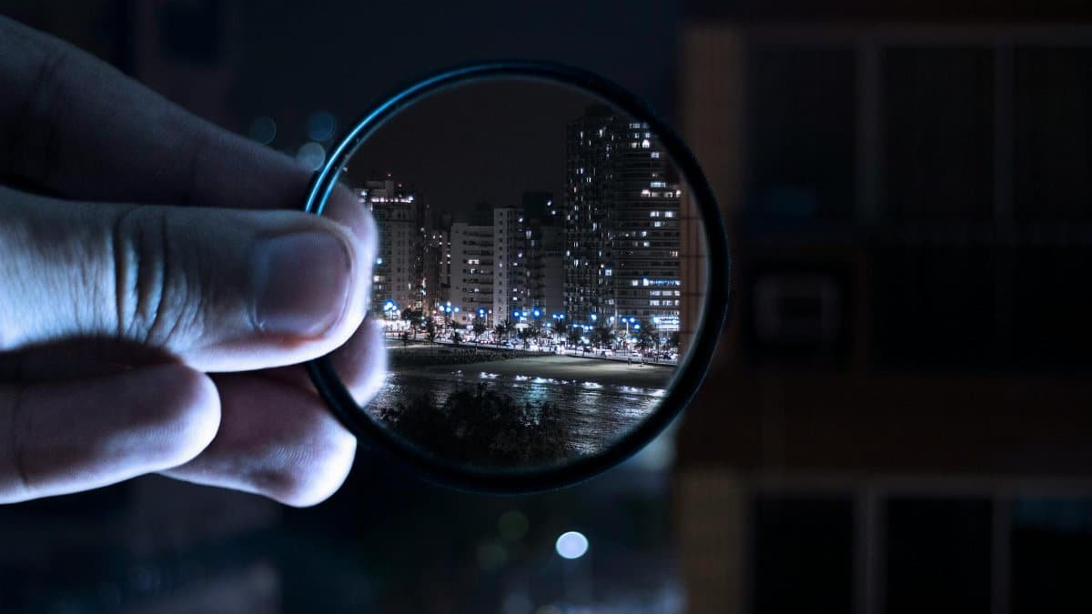 A hand holding a lens filter enhances a vibrant city nightlife scene.