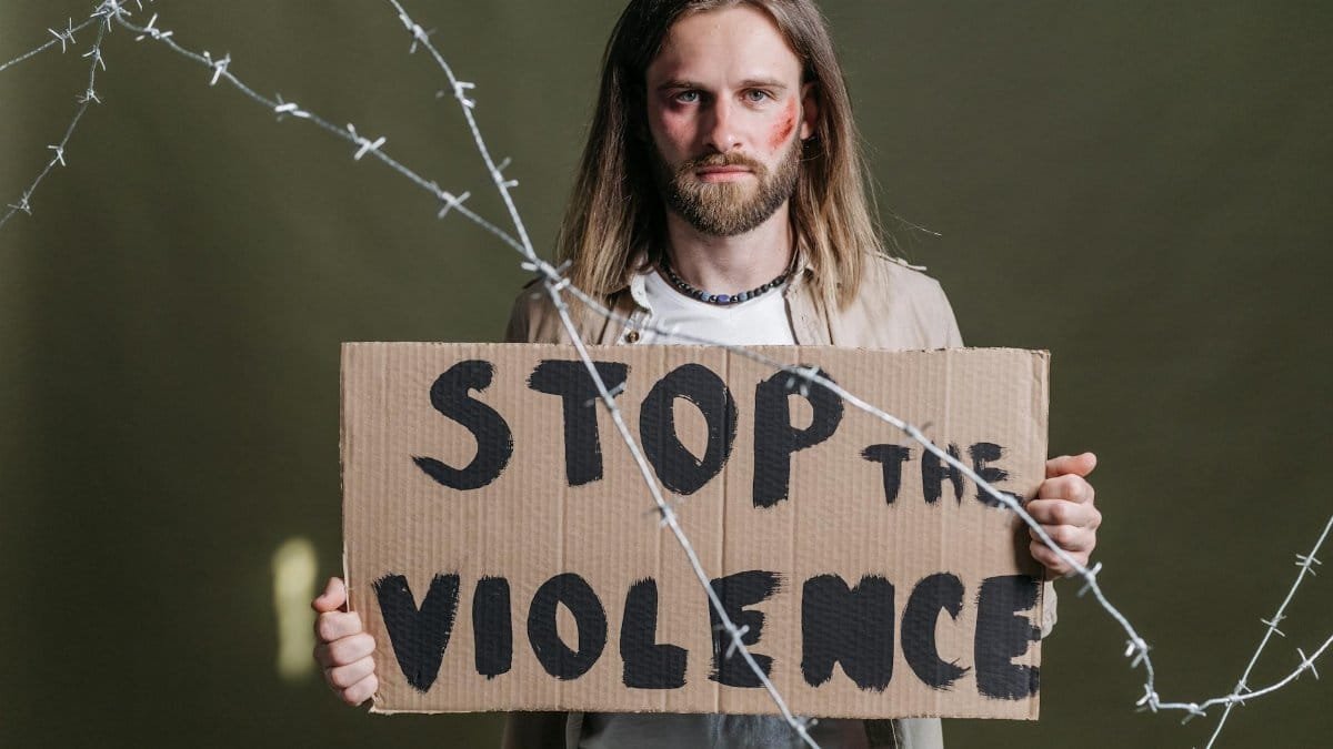 Man holding a 'Stop the Violence' sign with barbed wire emphasizing peace and protest.