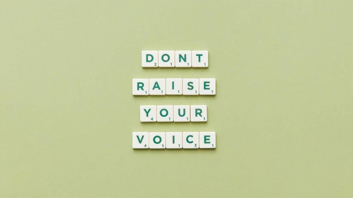 Scrabble tiles spelling 'Don't Raise Your Voice' on a green background.