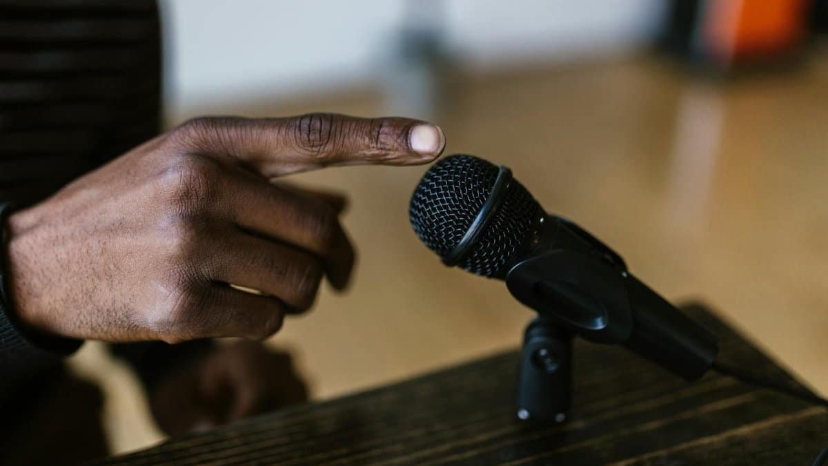 Close-up shot of a hand touching a microphone, ideal for audio, podcast themes.
