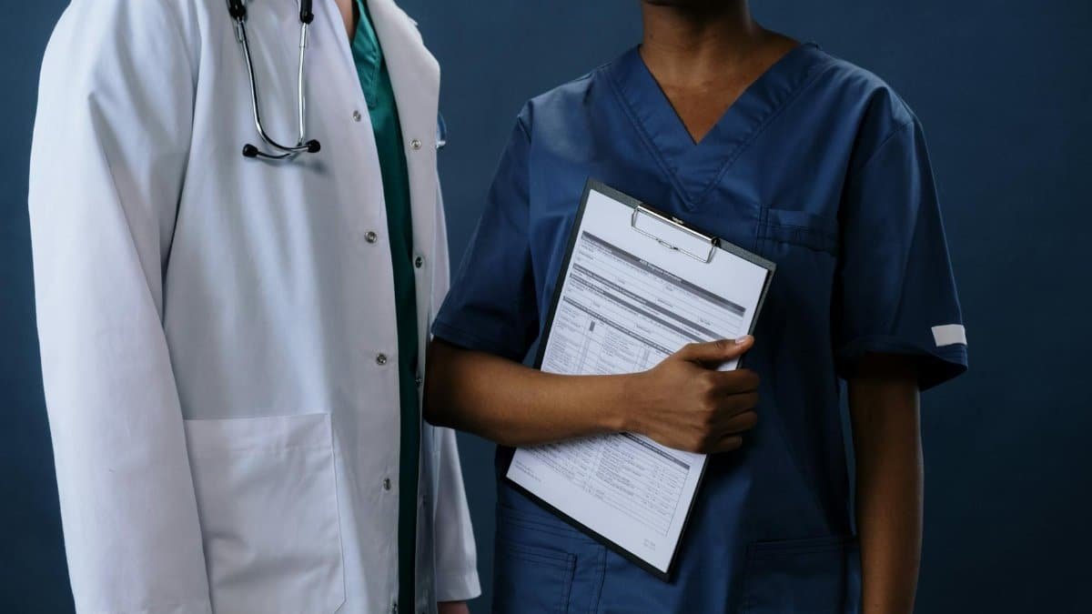 Two healthcare professionals in scrubs and lab coat with a clipboard, representing teamwork.