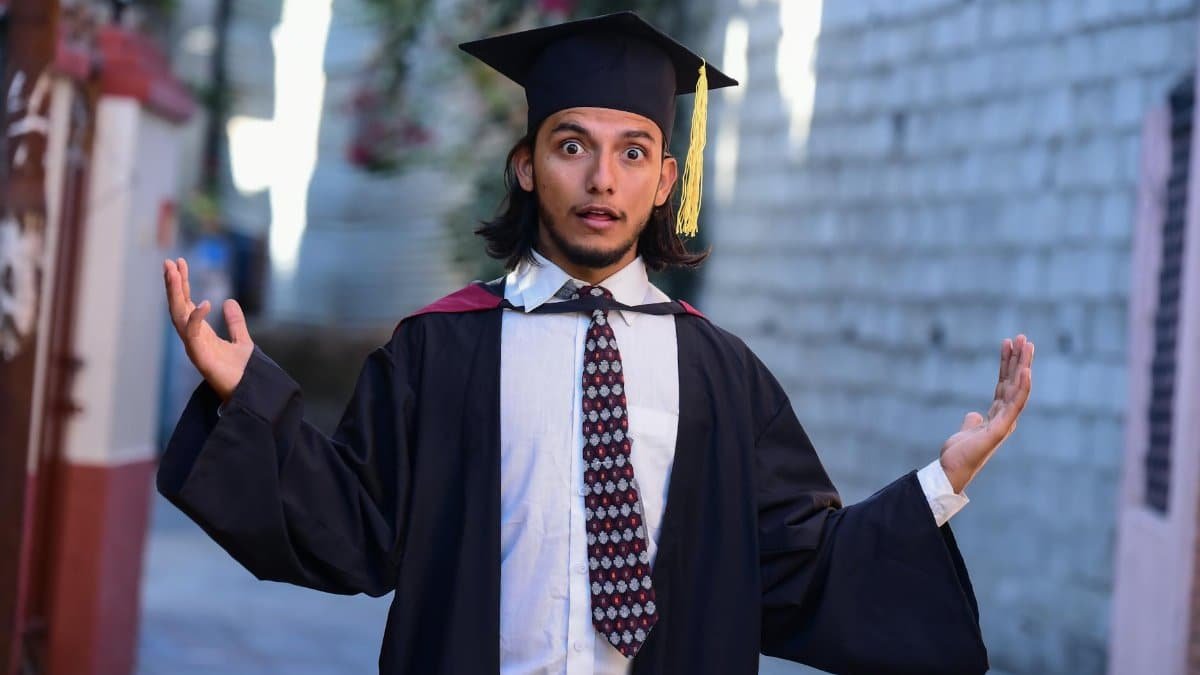 A surprised graduate poses outdoors in cap and gown, celebrating academic achievement.