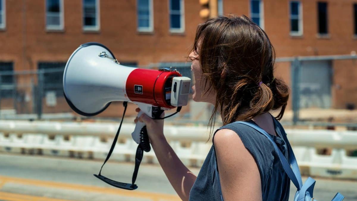 A young woman passionately speaking into a megaphone during a peaceful protest on a sunny day.