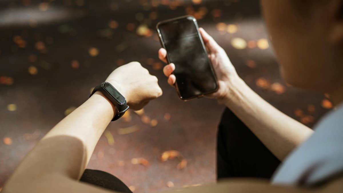 Back view of anonymous female using smartphone app and smart watch after jogging in park