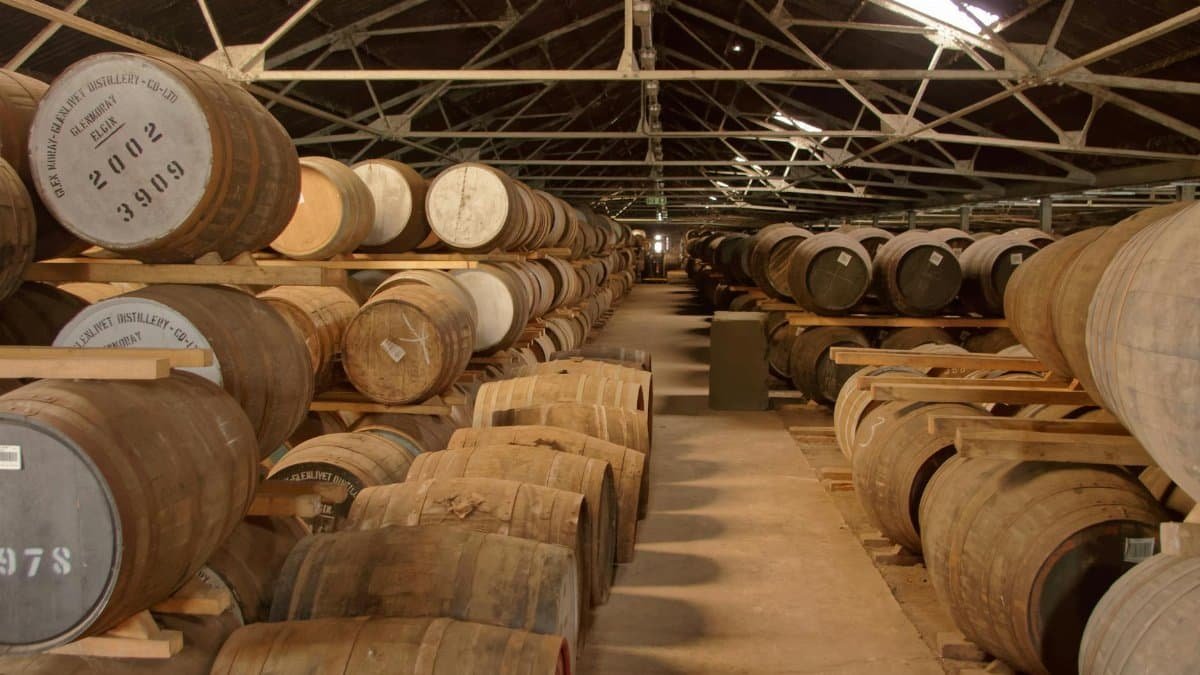 Rows of wooden barrels aging in a historic distillery warehouse, creating a rustic atmosphere.