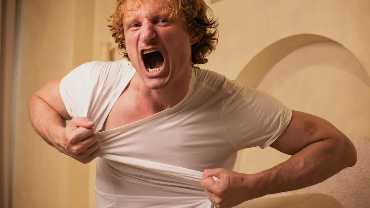 A man exhibiting anger and frustration by tearing his shirt indoors, with an intense expression.