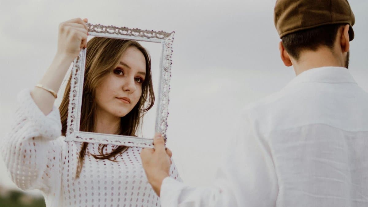 A woman posing with an ornate frame held by a man, outdoors in daylight.