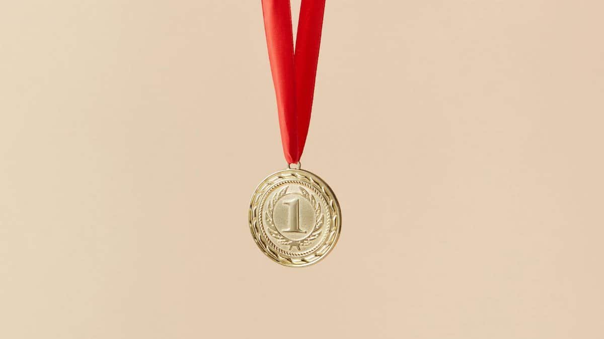 Close-up of a gold medal with a red ribbon on a beige background, symbolizing achievement.