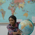 Teacher presenting a globe in front of a world map, enhancing geography education.