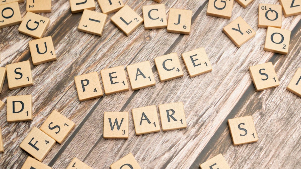 Wooden letter tiles spelling 'PEACE' and 'WAR' on a rustic surface.