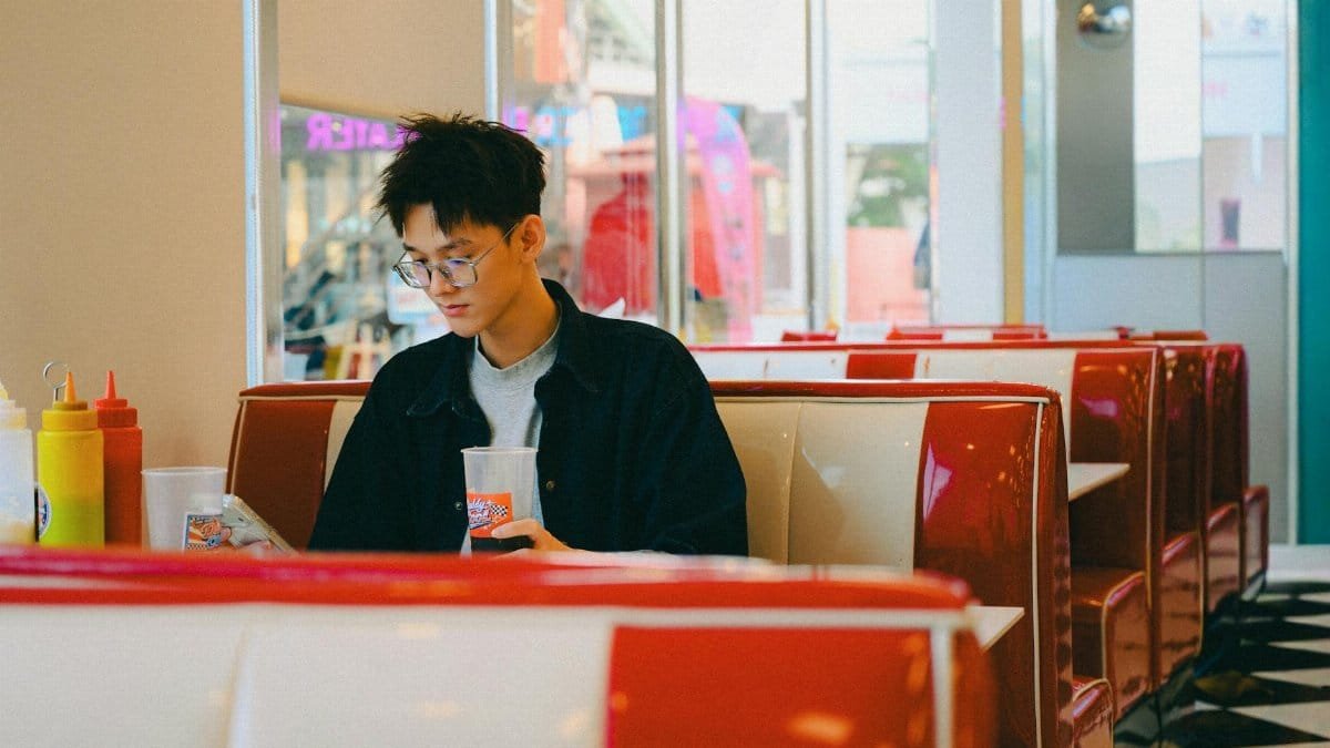 Young man enjoying a drink in a vintage style diner, browsing phone.