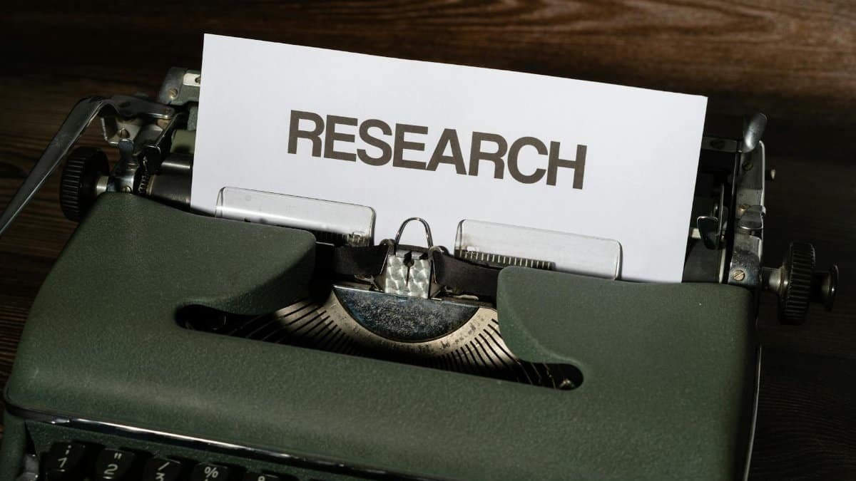 Close-up of a vintage typewriter with a paper labeled 'Research' inserted, on a wooden surface.
