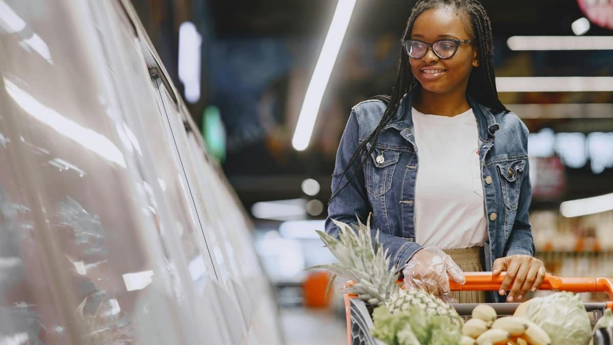Smiling woman with braided hair shopping in a supermarket with a full cart.