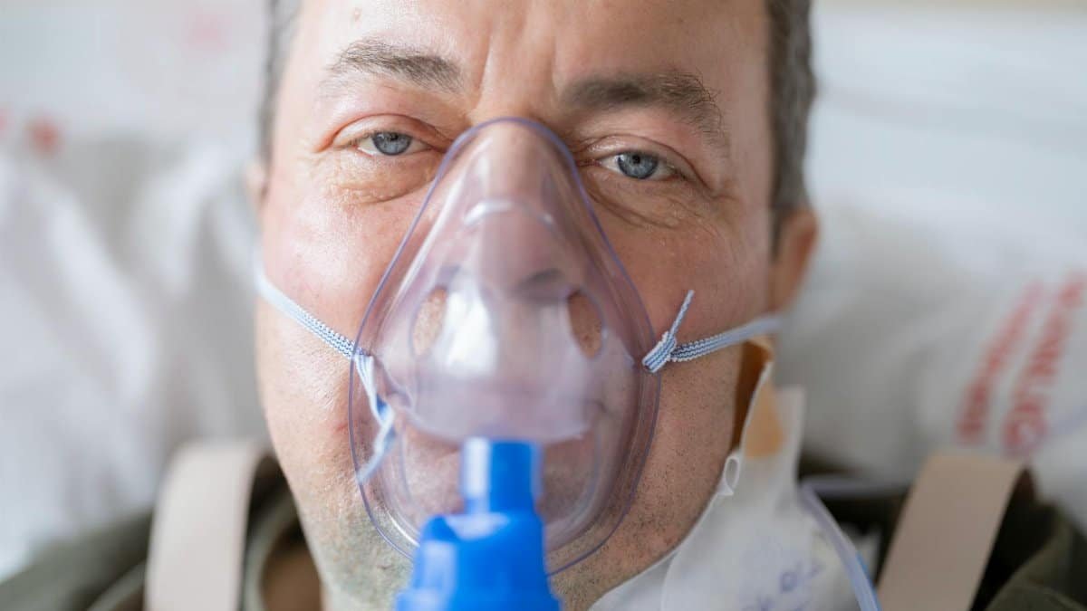Close-up of a man in a hospital bed wearing an oxygen mask, highlighting healthcare needs.