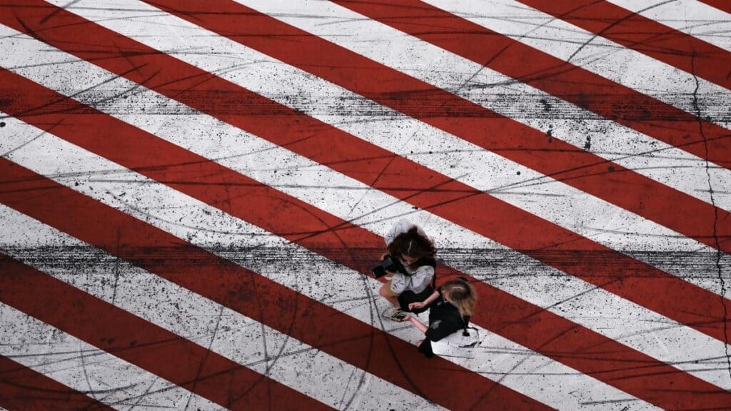 Aerial perspective on a crosswalk with bold red and white stripes, featuring two women walking.