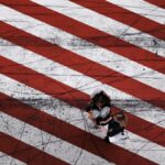 Aerial perspective on a crosswalk with bold red and white stripes, featuring two women walking.