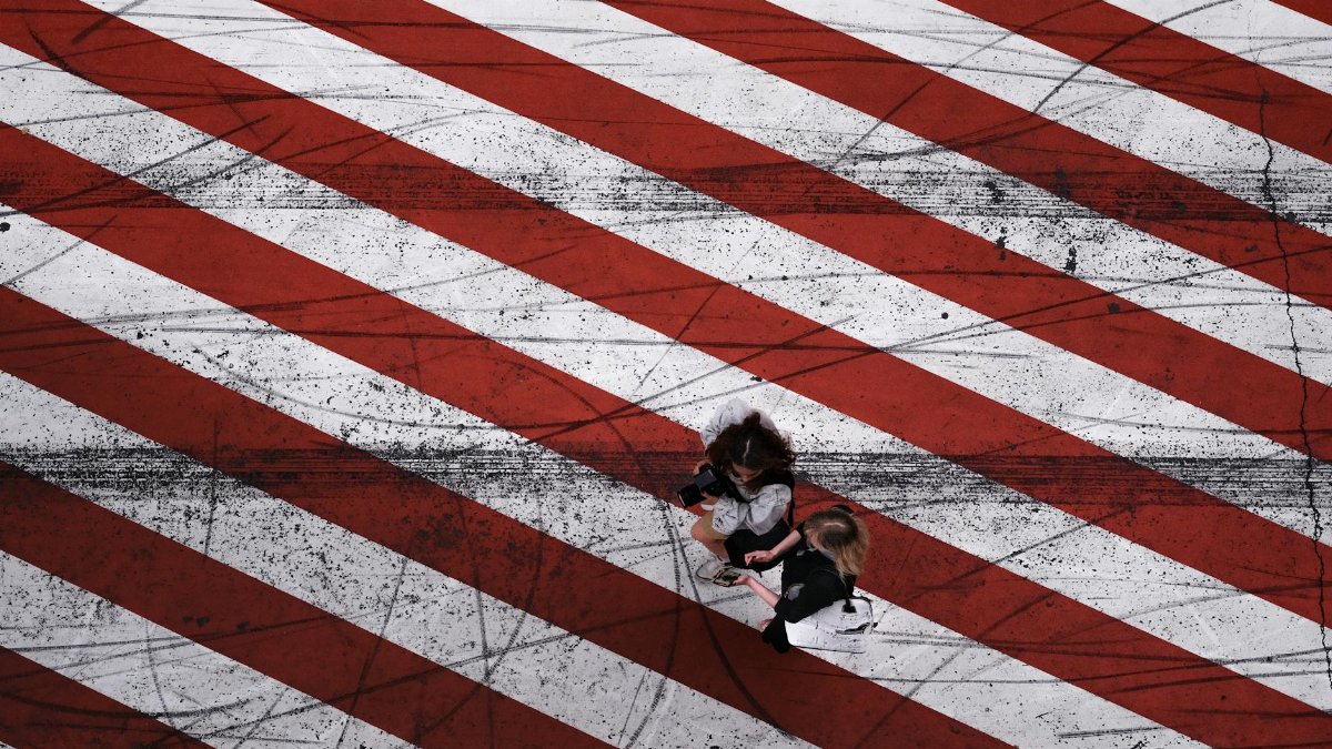 Aerial perspective on a crosswalk with bold red and white stripes, featuring two women walking.