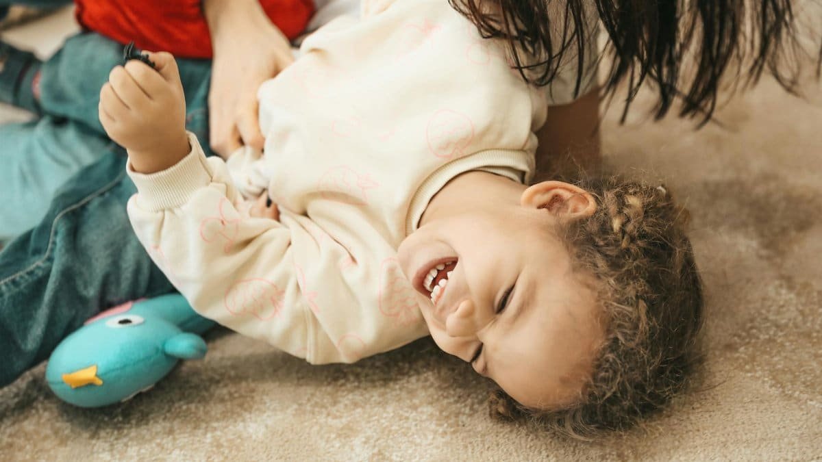 A happy child laughs while playing with a parent indoors, capturing pure joy and innocence.