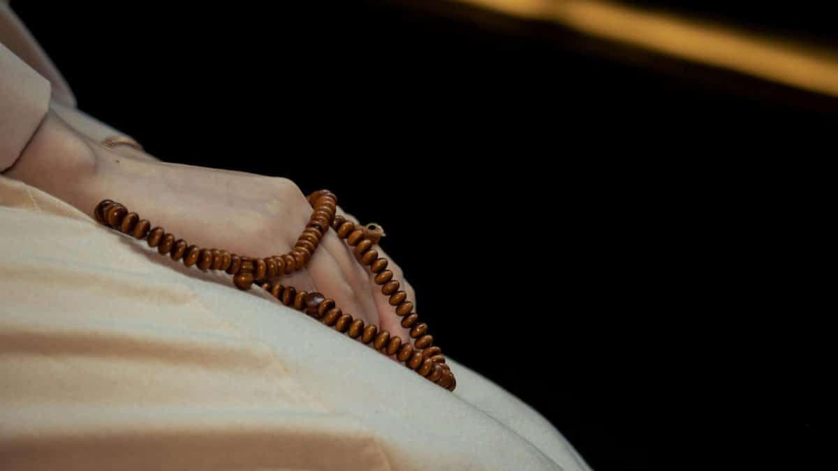 A woman's hand gently holding a wooden rosary against a dark background, symbolizing faith and spirituality.