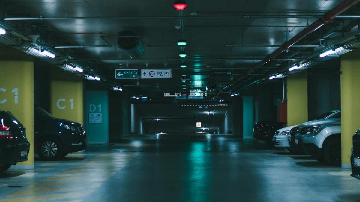 A dimly lit underground parking garage featuring parked vehicles and directional signs in Budapest.