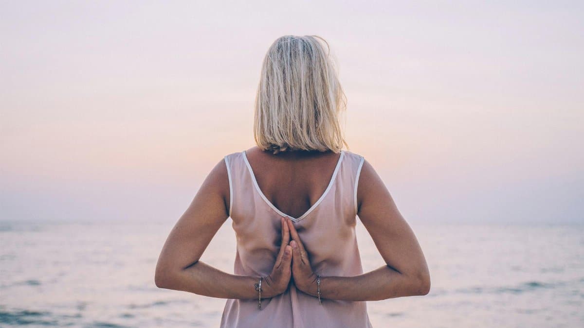 Back view of a woman meditating on a tranquil beach at sunset, promoting relaxation and mindfulness.