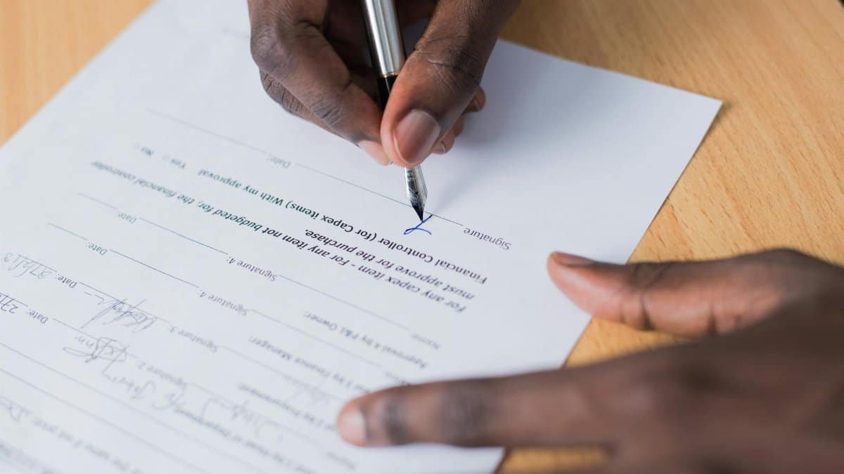 A close-up view of a person's hand signing a business contract on a desk with a pen.