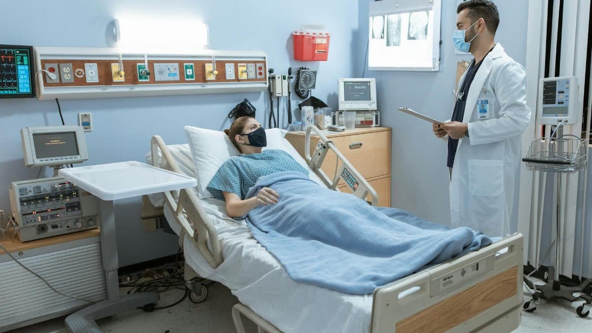 A doctor checking on a patient in a hospital room, both wearing face masks for safety.