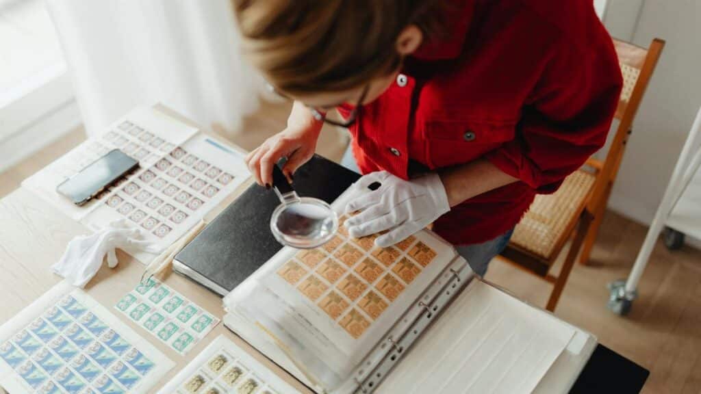 Woman in red reviewing postage stamps with a magnifying glass indoors.