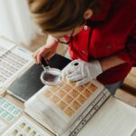 Woman in red reviewing postage stamps with a magnifying glass indoors.
