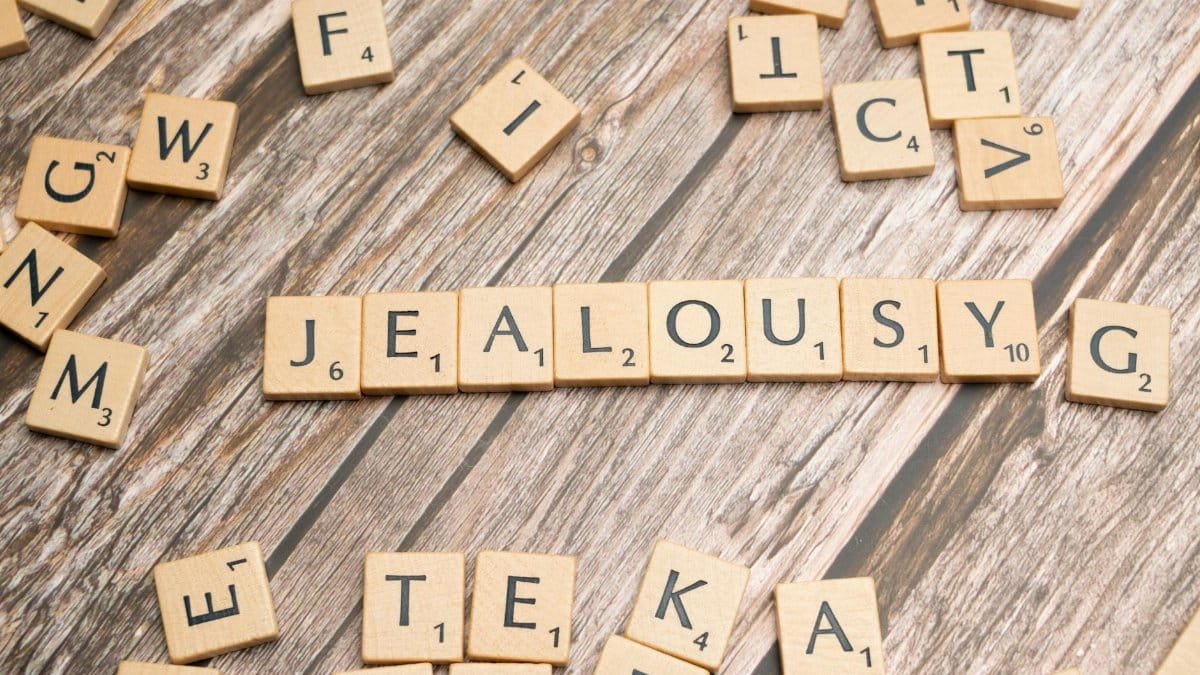 Wooden Scrabble letter tiles forming the word 'Jealousy' on a rustic wooden surface.