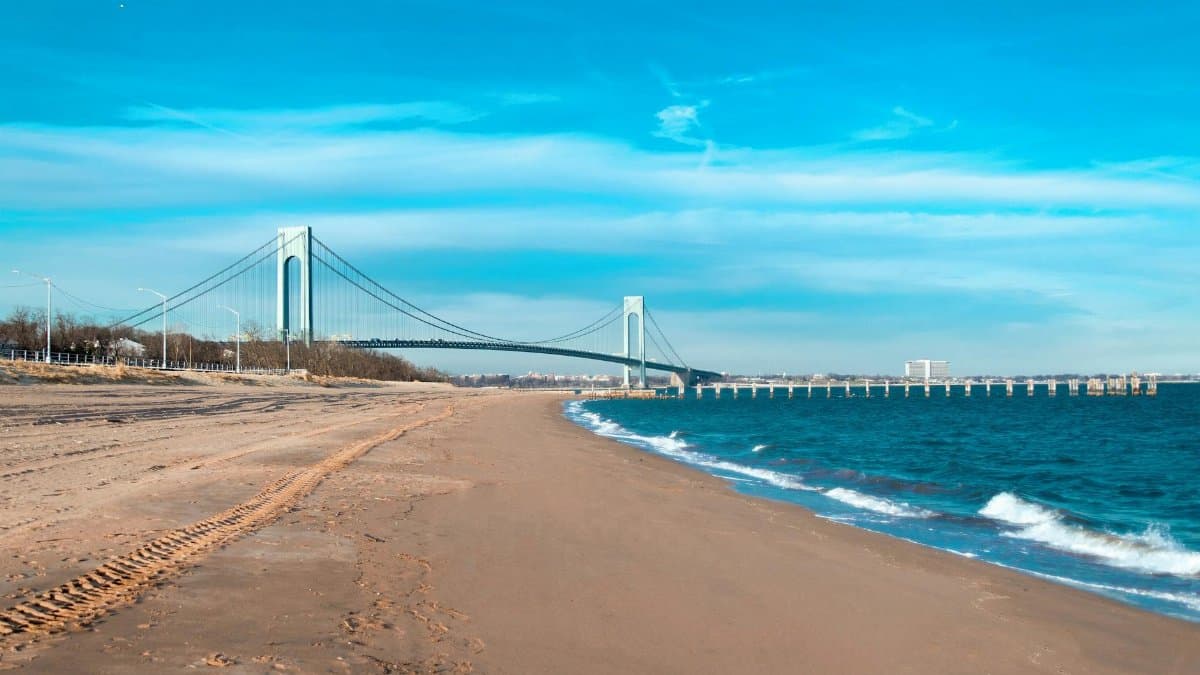 Scenic view of Verrazzano-Narrows Bridge spanning the coastline of Staten Island under clear blue skies.
