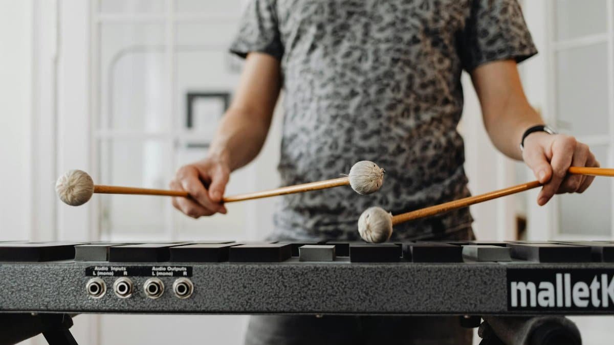 Adult musician practicing on a xylophone with mallets indoors, focusing on rhythm and technique.