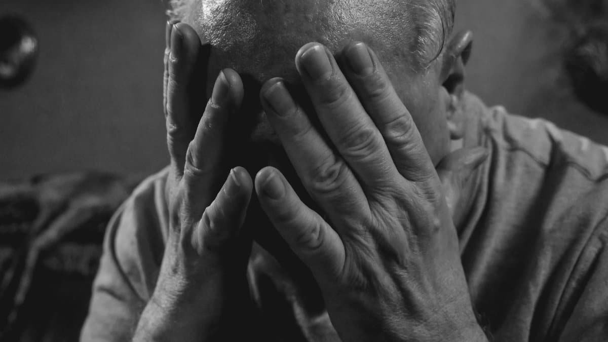 Elderly man covering face with hands, evoking emotions of sadness and stress.