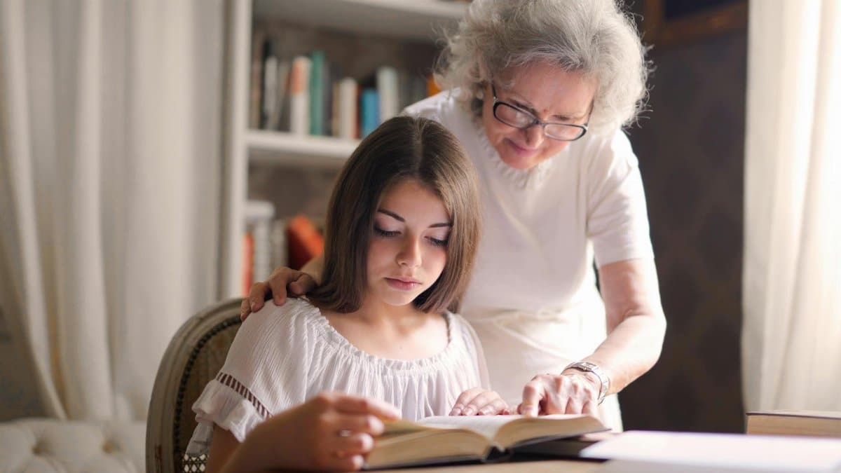 A grandmother and young girl reading a book together in a cozy indoor setting, fostering education and bonding.