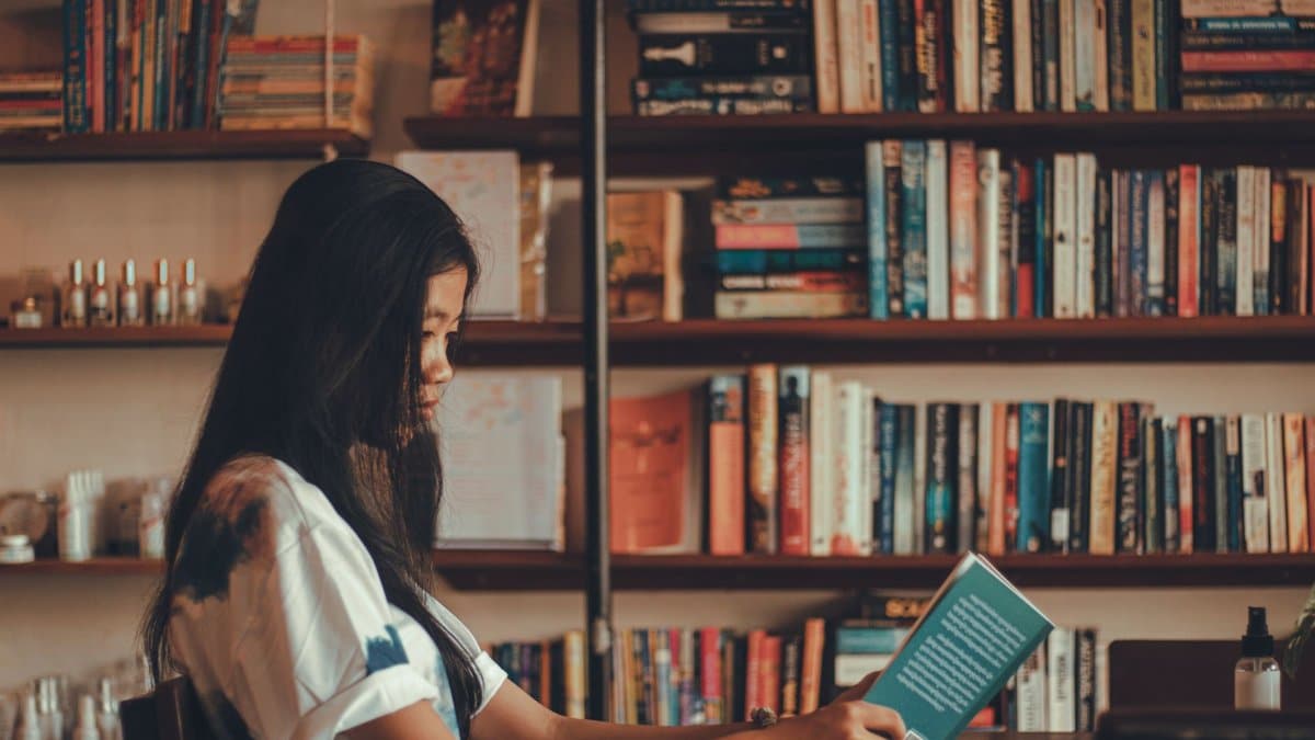 A young woman reads a book in a comfortable library with shelves full of books, offering a serene setting for relaxation.