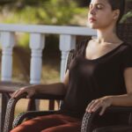 A woman in meditation with eyes closed sitting on a chair outdoors in the sunlight.