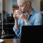 Woman in formal wear having coffee break from work at laptop in modern office