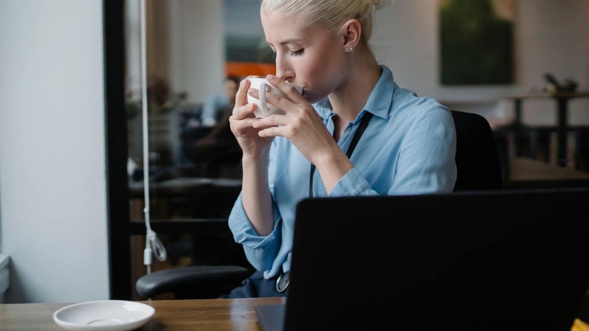 Woman in formal wear having coffee break from work at laptop in modern office
