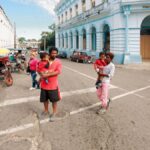 Street view with people walking near a historic blue building on a sunny day.