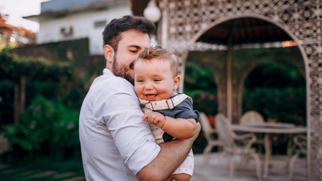 A father joyfully holds his baby in an outdoor garden. Capturing love and happiness.