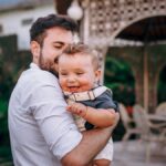 A father joyfully holds his baby in an outdoor garden. Capturing love and happiness.