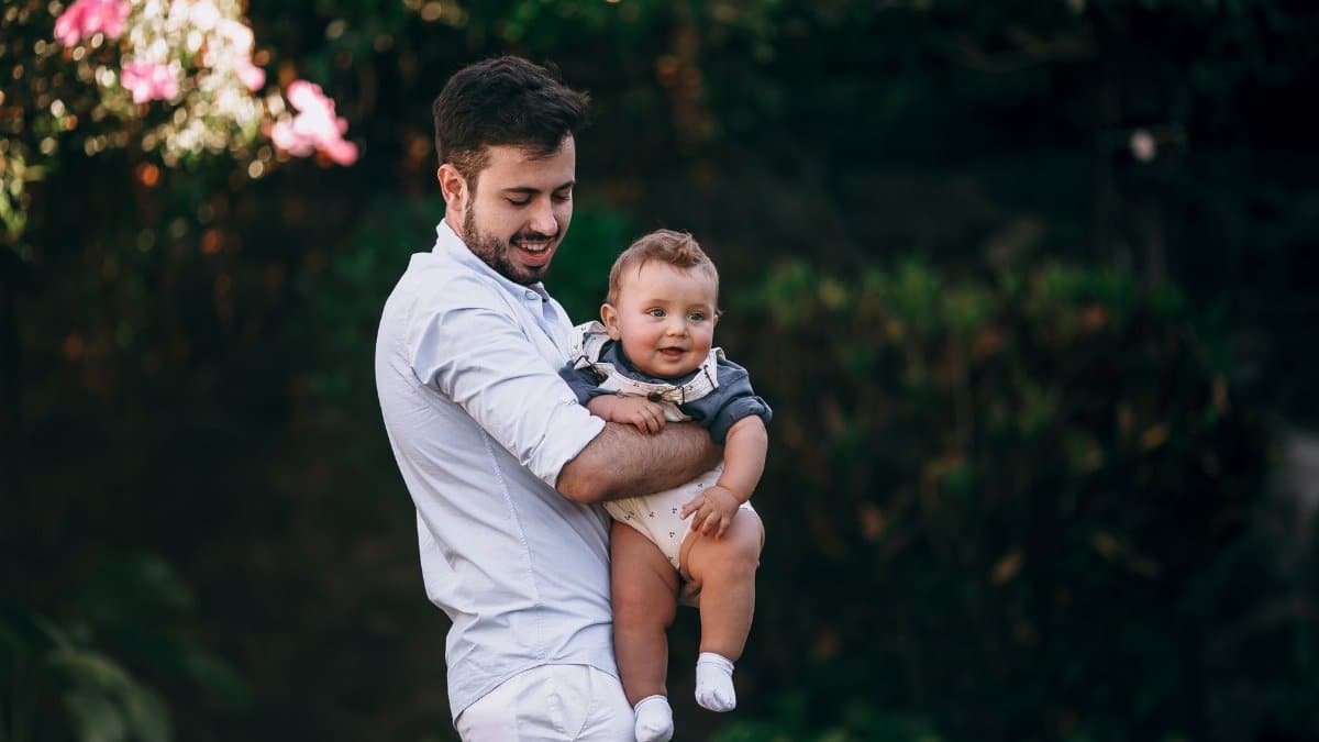 A joyful father holds his baby while standing in a lush garden, capturing a heartwarming outdoor moment.