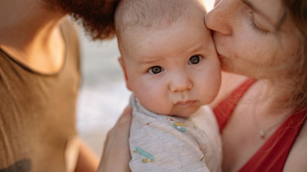 A tender moment of parents kissing their baby, highlighting love and family bonds.