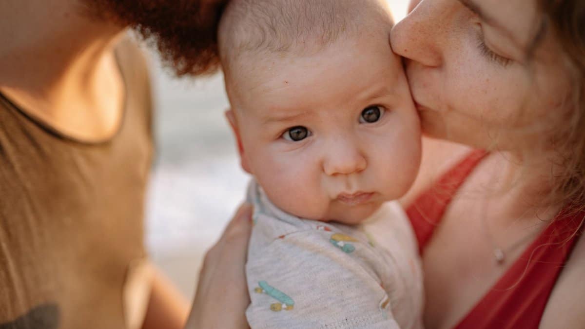 A tender moment of parents kissing their baby, highlighting love and family bonds.