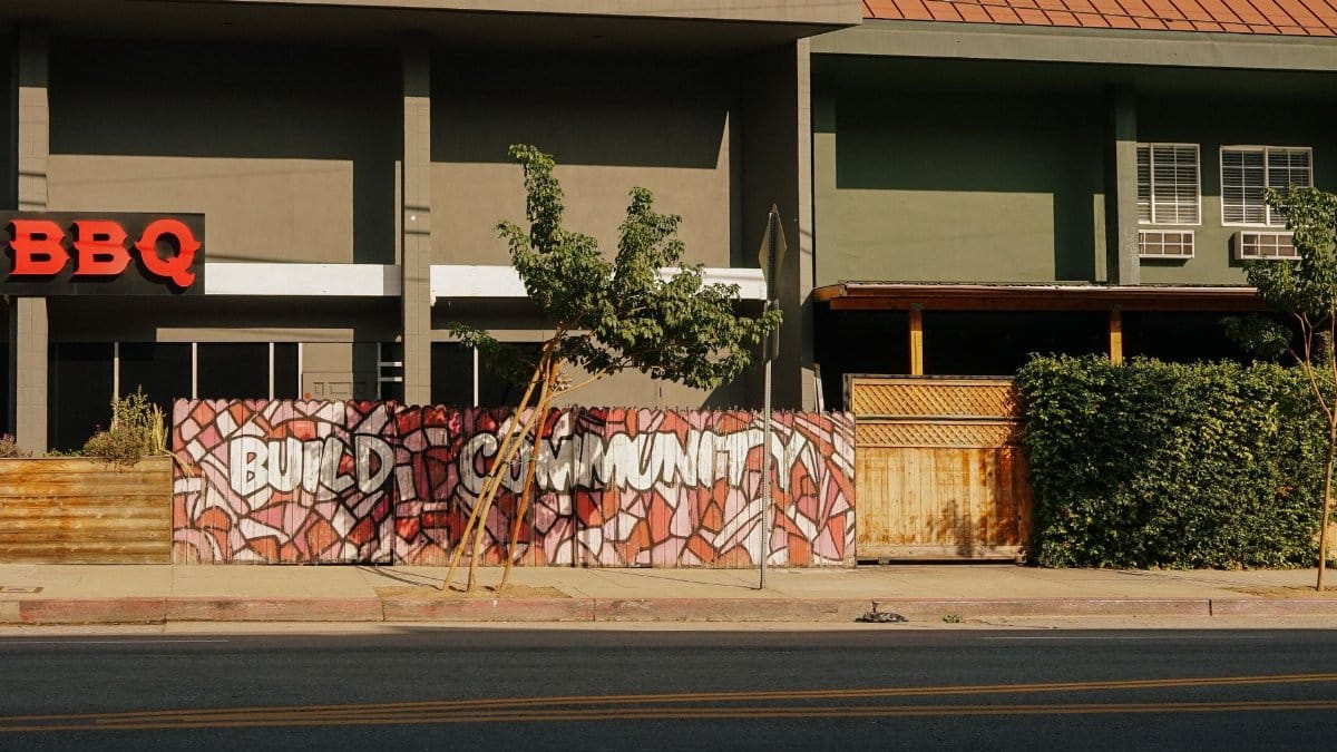 Graffiti mural with 'Build Community' on a city street near a BBQ restaurant.