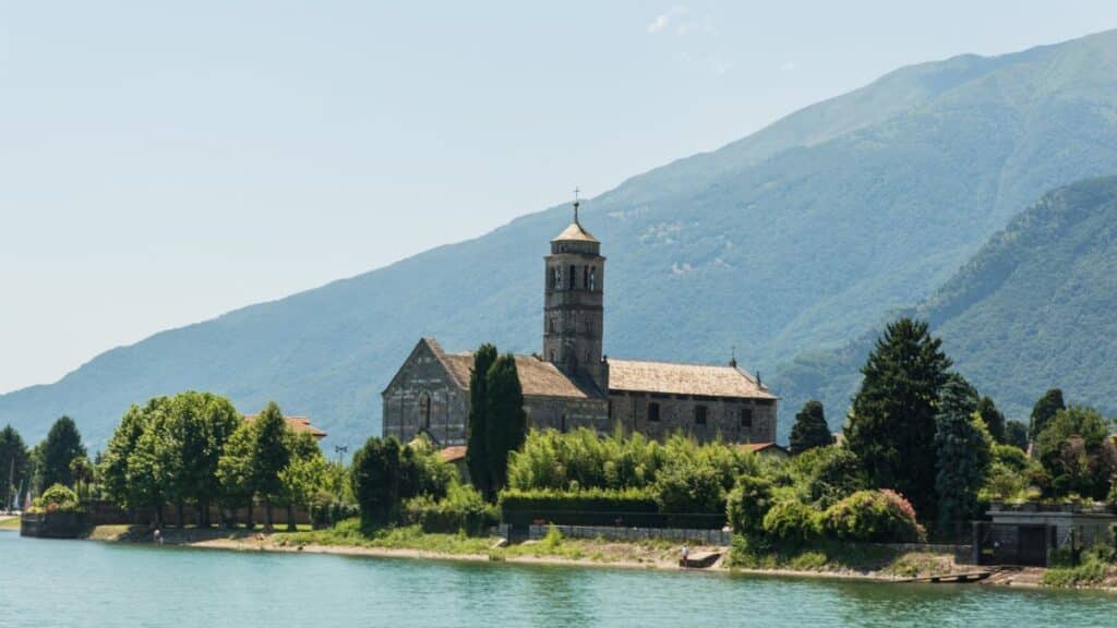 Scenic view of a historic church on Lake Como's shore in Lombardy, Italy, surrounded by lush greenery.