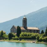 Scenic view of a historic church on Lake Como's shore in Lombardy, Italy, surrounded by lush greenery.